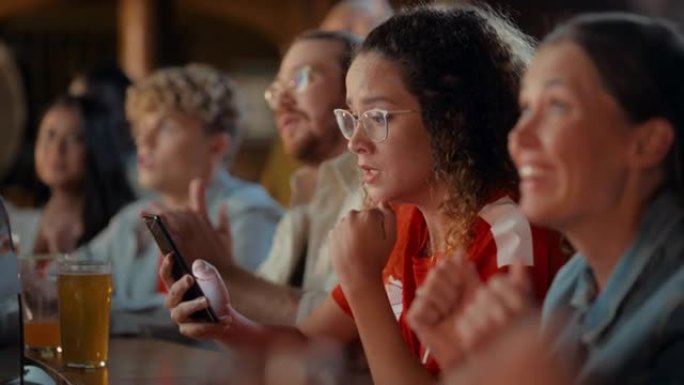 一位穿着红色球衣的多民族女性使用智能手机的肖像，对她最喜欢的足球队的体育赌注感到紧张。足球队进球时充