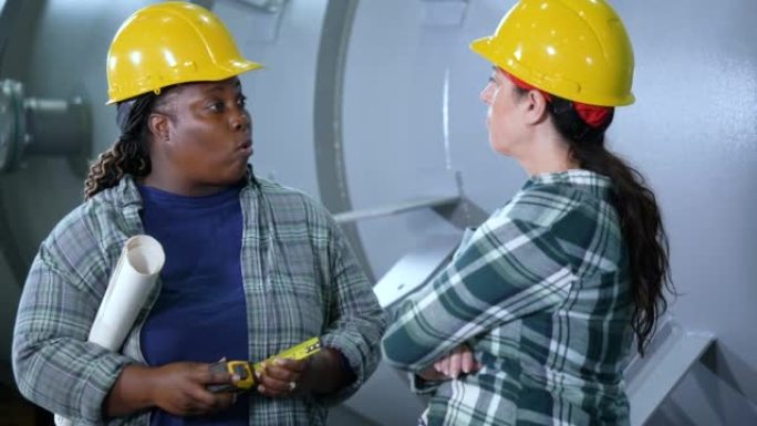 Two women working in metal fabrication plant, talk