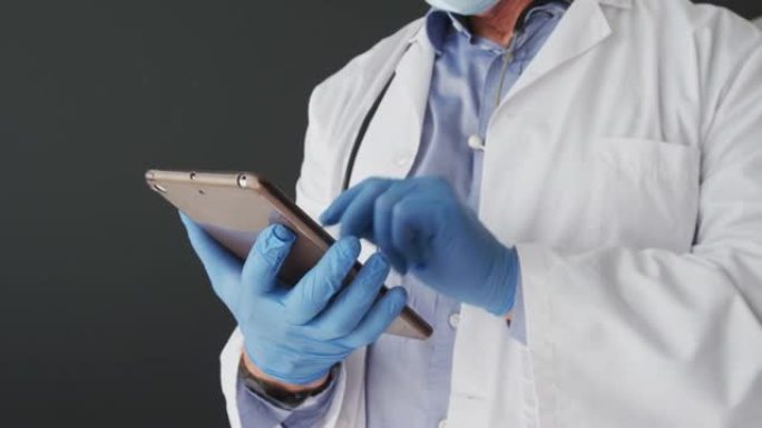 使用数字平板电脑戴着手术手套的高加索男性医生的中段