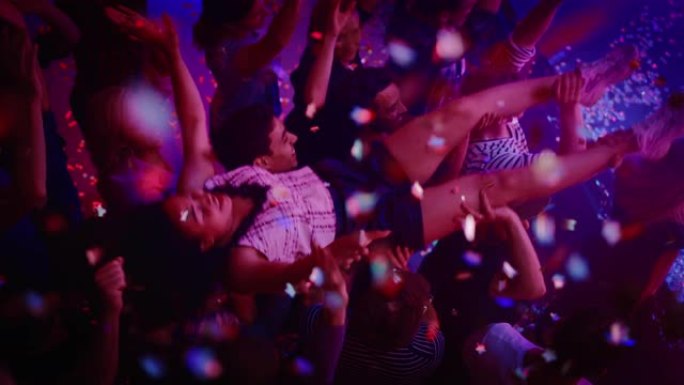 在夜总会的一场音乐会上，音乐节的观众举起手来。歌迷们举起一个女孩，为乐队欢呼。明亮多彩的频闪灯营造气