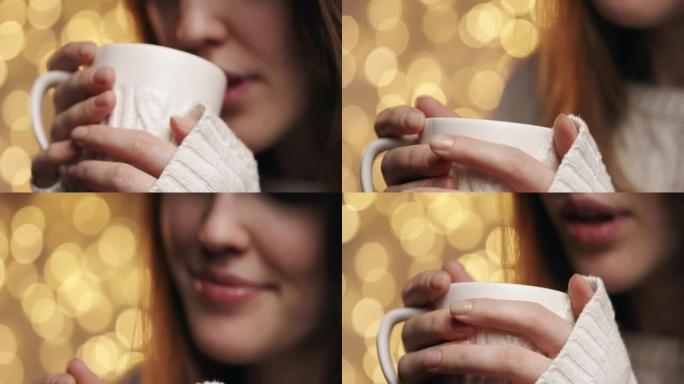 一个从白色杯子里喝可可的女孩的脸的特写镜头，用双手握住它
