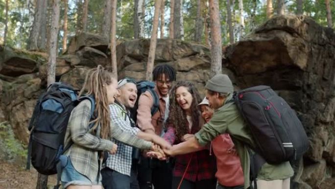 一群朋友游客聊天，然后携手表达团结和团结站在森林里