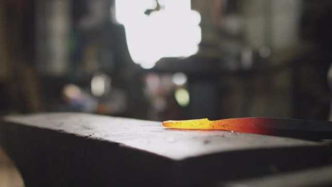 男性铁匠在铁砧上锤击红色热金属制品的特写