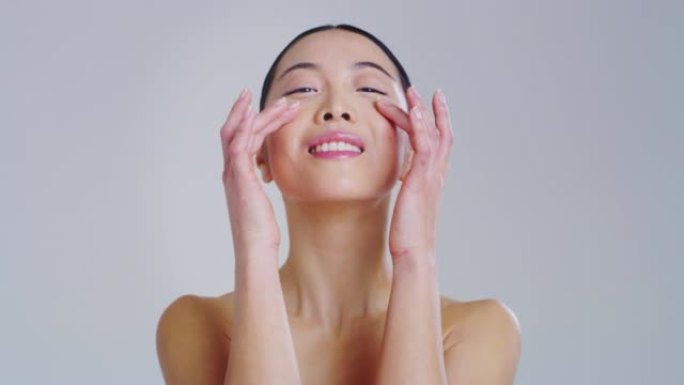 亚洲女人的慢动作，拥有美丽的脸庞和完美的皮肤，刚刚从杂质中清洗干净，用手指轻轻呵护它，为白天或晚霜做