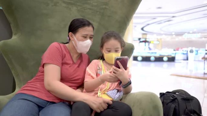带手术口罩的母女在购物中心享受智能手机