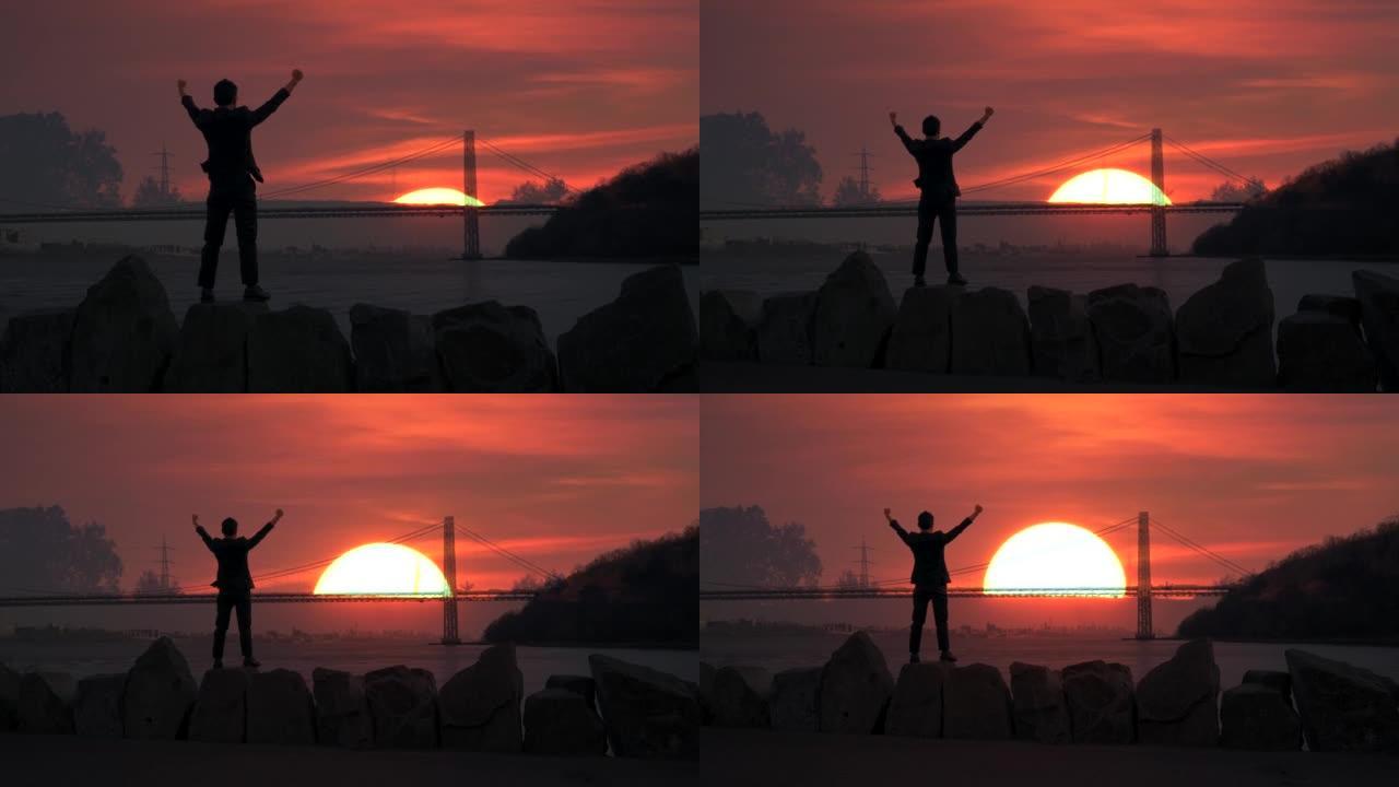 一名男子站在户外，双臂举起，做着胜利的姿势，在早晨的日出中展示了成功的生活方式