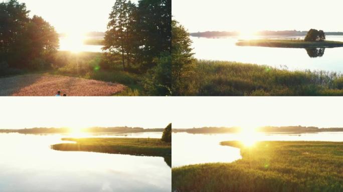 无人机在湖岸向小岛低空飞过男人和女人，令人难以置信的镜头在平静的水面上闪耀日出