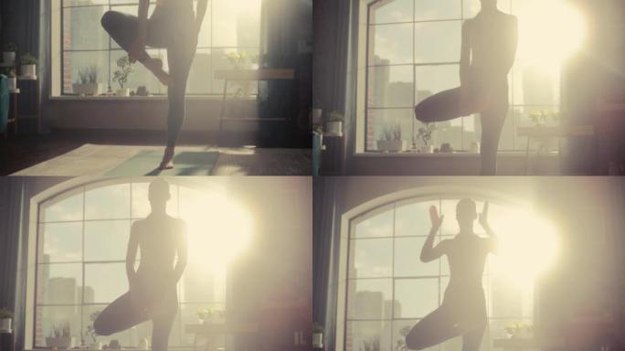 年轻美丽的女性锻炼身体，在树木瑜伽中保持平衡，早上在她阳光明媚的阁楼公寓里摆姿势。健康的生活方式、健