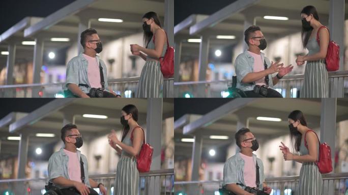 旅游亚洲华裔男子坐轮椅晚上在城市街与他的女性朋友交谈