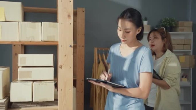 专业迷人开朗的两个亚洲女士老板少年与休闲持有平板电脑检查库存产品控制送货到客户订单站在家里的布店。