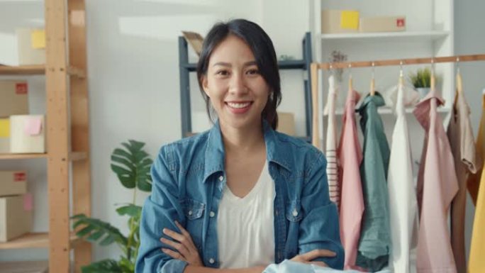 年轻的亚洲女士时装设计师的肖像在家庭办公室工作时感到幸福的微笑，双臂交叉，看着相机。