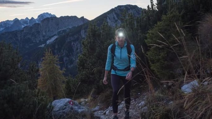 年轻的女徒步旅行者在黄昏时带着头灯在落基山小径上徒步旅行时欣赏风景