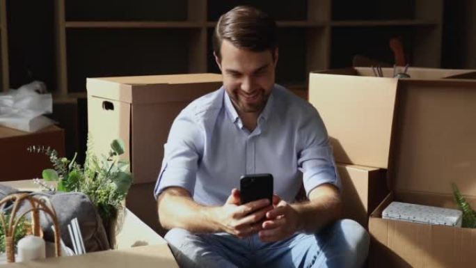 男子在搬迁时使用智能手机坐在装有物品的盒子附近