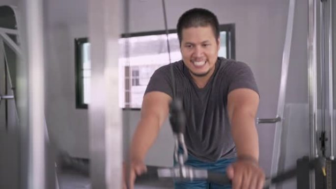 亚洲男子使用训练机锻炼背部肌肉在健身房锻炼