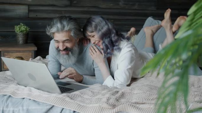 男人和女人用笔记本电脑躺在床上说话和笑的慢动作