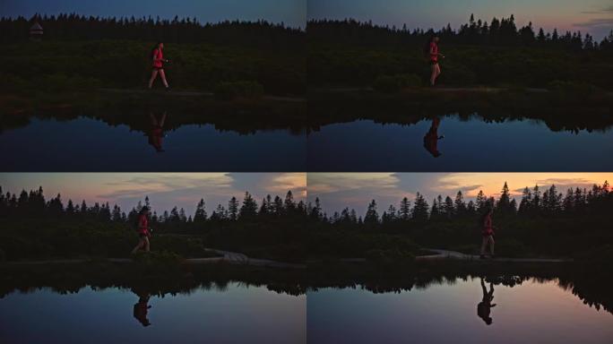 慢动作的年轻背包客黄昏时在池塘边的小径上行走
