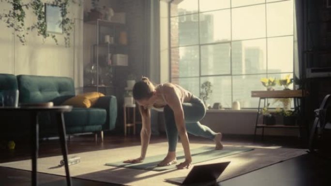 年轻的运动女子早上在阳光明媚的家庭客厅锻炼、伸展和练习瑜伽。通过笔记本电脑进行在线健身训练锻炼。