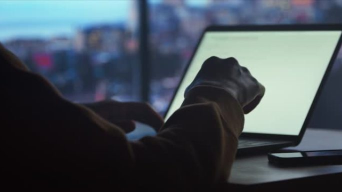 一个穿着黄色连帽衫的年轻人坐在黑暗的房间里，在笔记本电脑上打字，工作到很晚