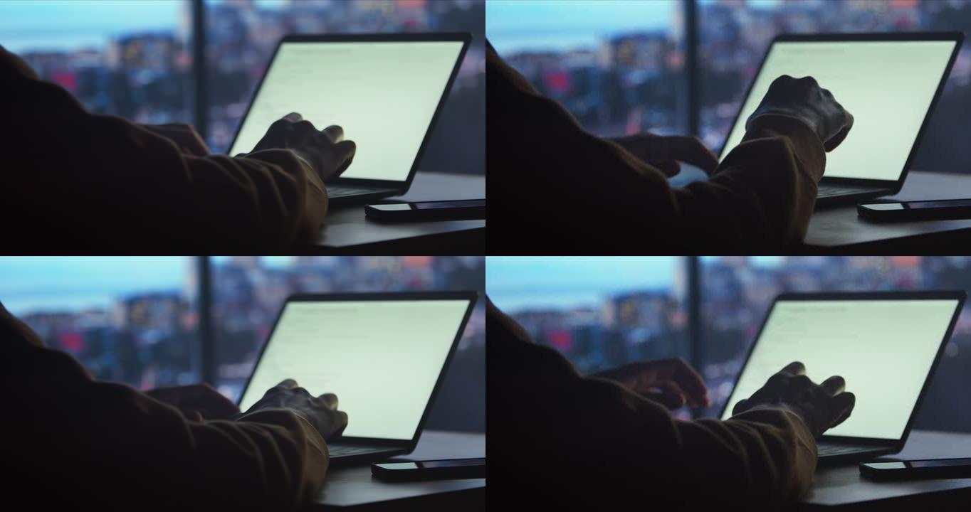 一个穿着黄色连帽衫的年轻人坐在黑暗的房间里，在笔记本电脑上打字，工作到很晚