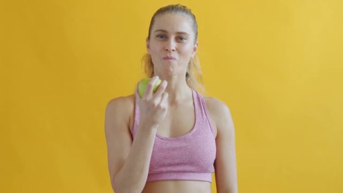 可爱的女运动员吃苹果享受黄色背景下的新鲜水果