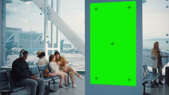 机场航站楼: 绿屏广告广告牌，带色键的到达显示，模拟广告空间。背景: 不同的人群在航空枢纽的登机休息