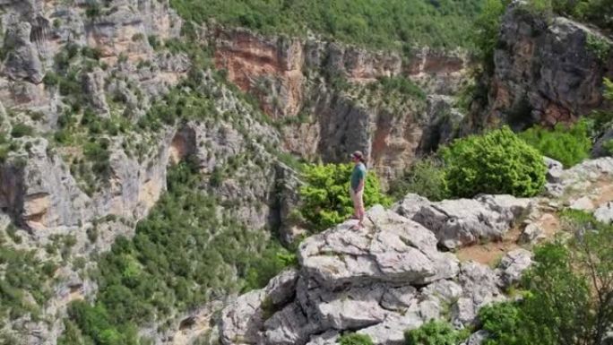 人站在悬崖边，环顾四周。在峡谷深处的岩石上绕着旅行者飞行。成功，目标实现概念。空中无人机射击