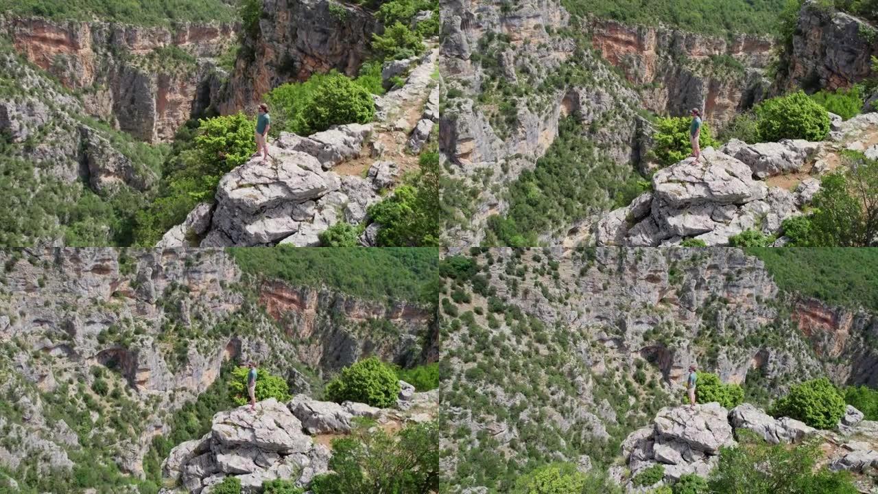 人站在悬崖边，环顾四周。在峡谷深处的岩石上绕着旅行者飞行。成功，目标实现概念。空中无人机射击