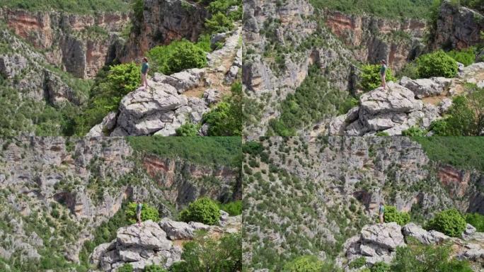人站在悬崖边，环顾四周。在峡谷深处的岩石上绕着旅行者飞行。成功，目标实现概念。空中无人机射击