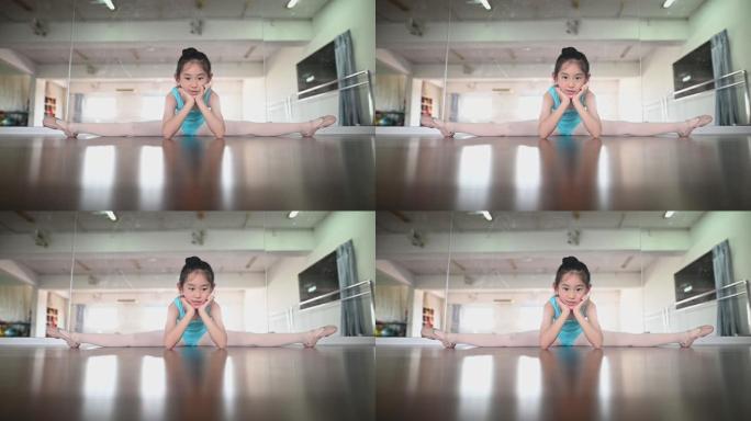 坐在地上的亚洲中国年轻女孩在舞蹈室里看着相机微笑