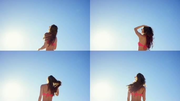 4k视频片段，一个无法识别的女人独自站在沙滩上玩头发
