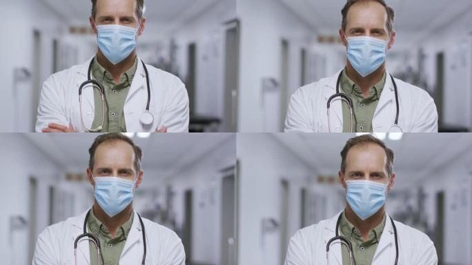 医院走廊上双臂交叉戴着口罩的白人男性医生的肖像