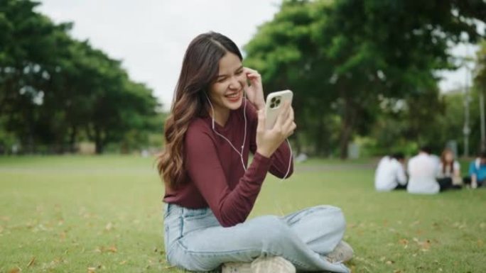 美丽的女孩在绿色公园使用智能手机在耳机中听音乐