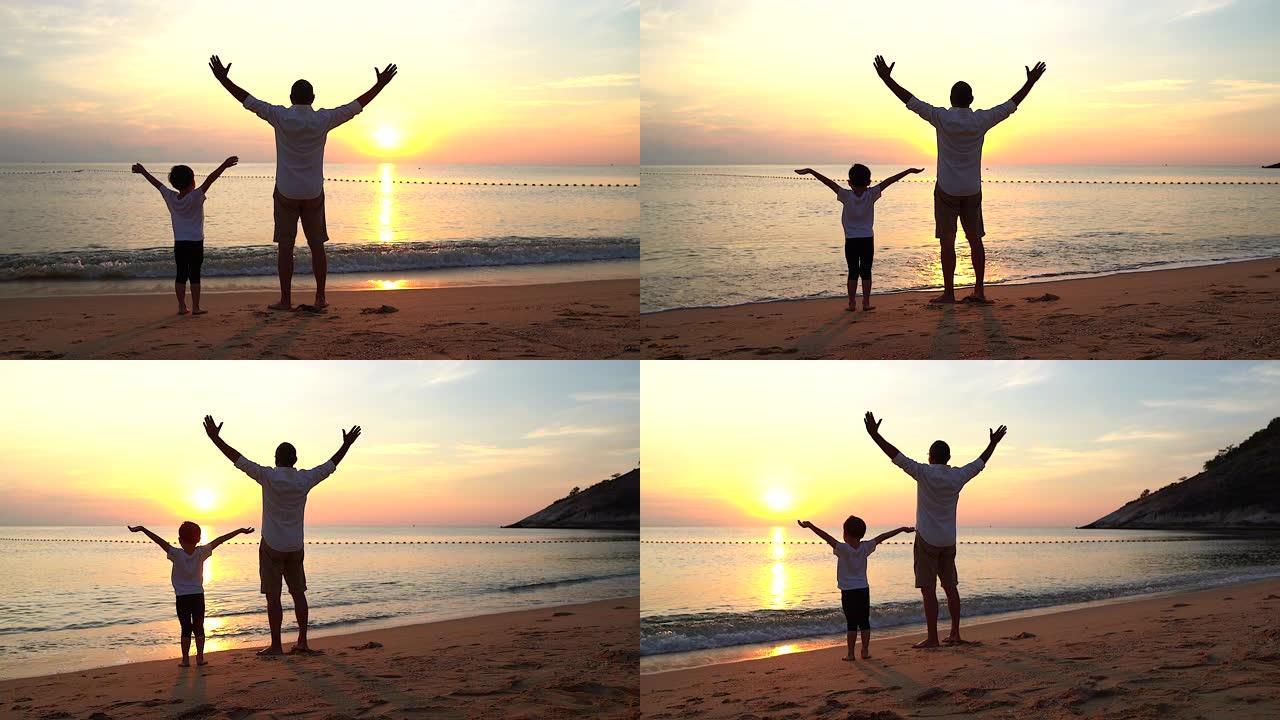 父亲和儿子在日出时站在海滩上，他们一起度过了美好的家庭时光。用慢动作摄像机拍摄。