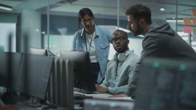 现代办公室中多元化的多民族团队: IT程序员的团队合作聚集在台式计算机周围，交谈，寻找解决方案。专家