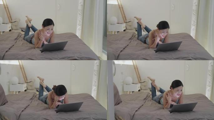 快乐的亚洲女人在床上使用笔记本电脑