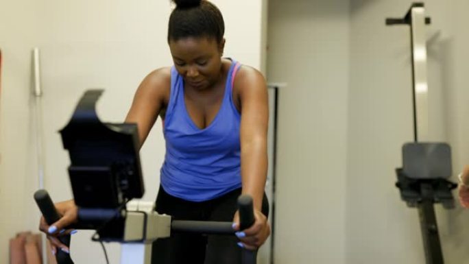 女人在健身房与私人教练一起在自行车机上锻炼