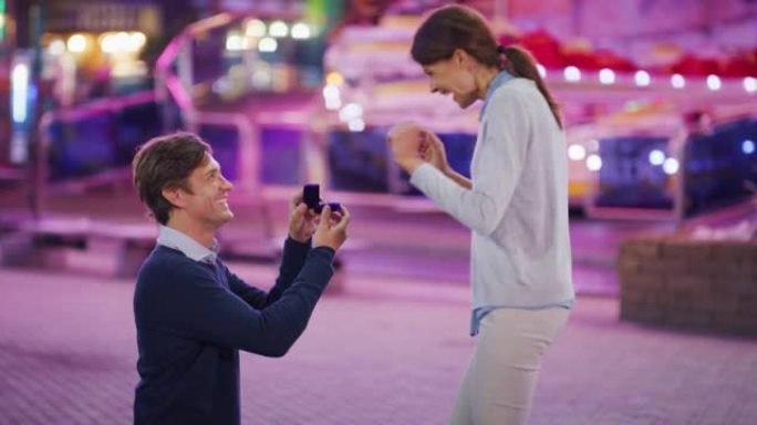 年轻英俊男子的真实特写镜头正在游乐园里用露娜公园的灯光向他心爱的女人求婚。