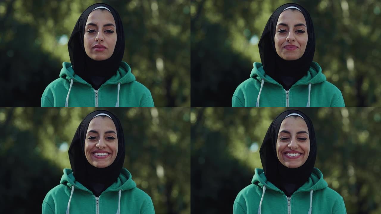 美丽的年轻阿拉伯女子微笑着绿色背景的肖像。带着头巾的快乐穆斯林女少年在公园享受新鲜空气，利用周末的空