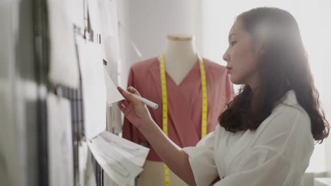 女时装设计师为她的项目选择草图并将其固定在墙上