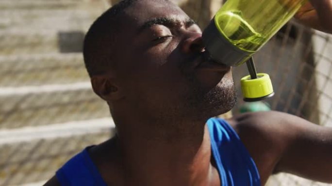 疲惫的非洲裔美国人坐在水瓶里喝水，在户外锻炼休息