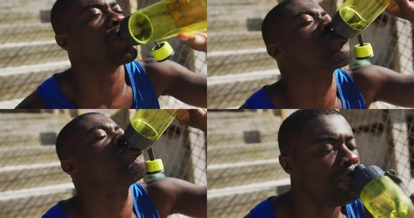 疲惫的非洲裔美国人坐在水瓶里喝水，在户外锻炼休息