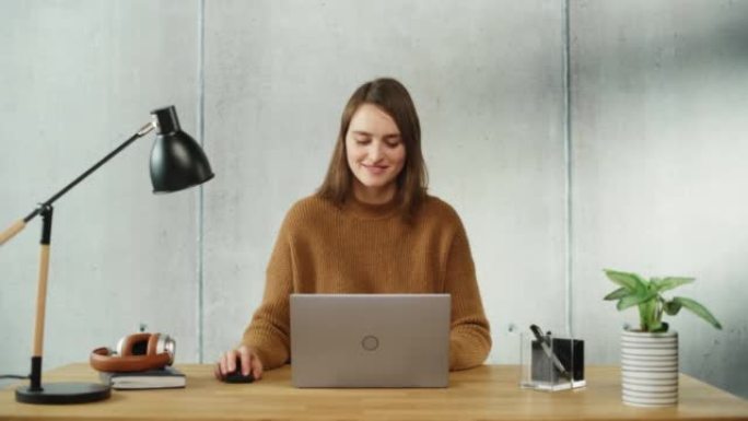 专业的创意女人坐在办公室的办公桌前，在笔记本电脑上工作。现代办公空间设计非常适合从事电子商务项目的生