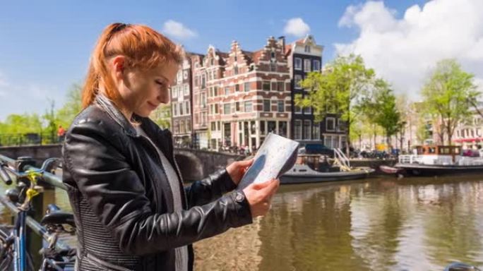 快乐的女人站在阿姆斯特丹运河旁边，拿着城市地图，欣赏美丽阳光明媚的日子里的景色