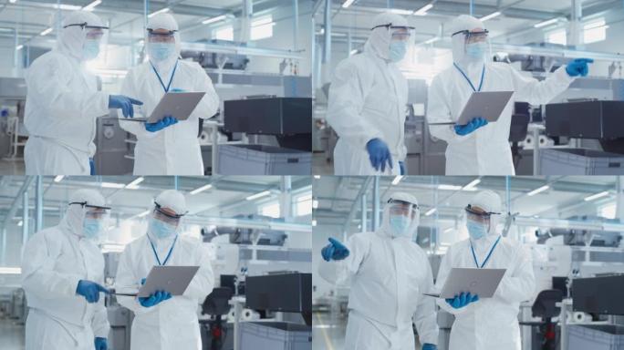 两名工程师站在一家重工业工厂的无菌工作服中，使用笔记本电脑，检查工业制造机器的设置并配置生产功能。