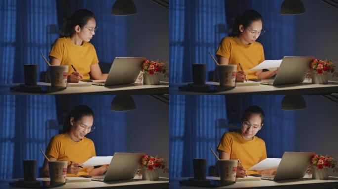 亚洲妇女坐在家里的办公桌上，深夜用笔记本电脑工作