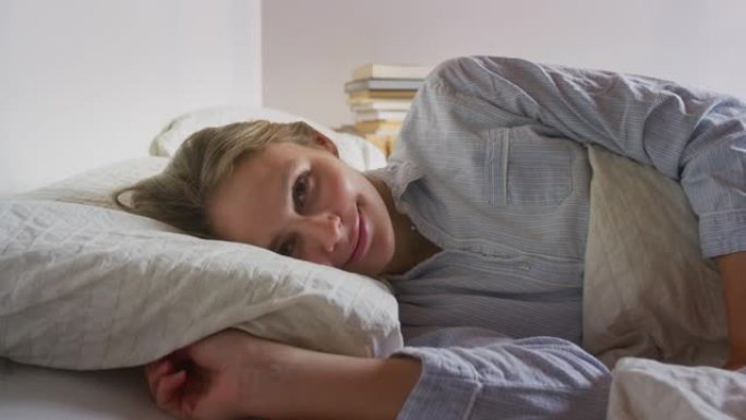 一个年轻的金发女人在一个温暖的羽绒被里安静舒适的睡觉后醒来的真实照片