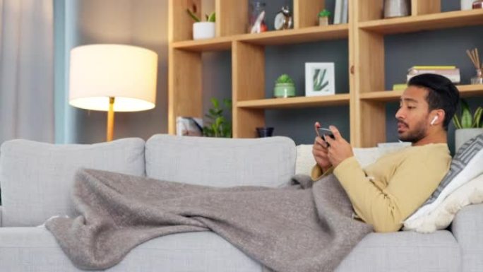 亚洲男子在家里独自在沙发上打哈欠和放松时，通过电话在线观看和流媒体电影或连续剧。疲惫的年轻男性在网上