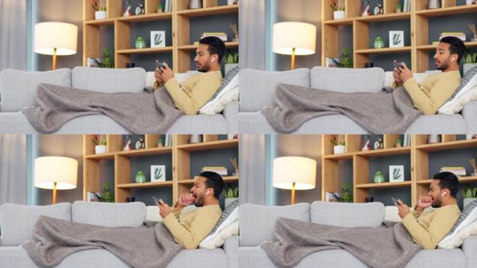 亚洲男子在家里独自在沙发上打哈欠和放松时，通过电话在线观看和流媒体电影或连续剧。疲惫的年轻男性在网上