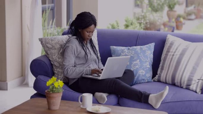 年轻的黑人千禧一代非洲女性，专业，自信，学生，家庭办公室，坐在沙发上，在家工作，笔记本电脑，现代技术