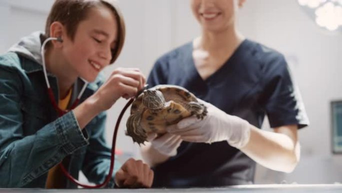 女兽医抱着一只乌龟，让宠物主人有机会通过医学听诊器听动物说话。男孩带着他的宠物去做定期检查